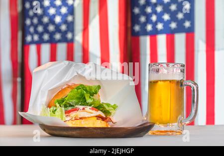 Delizioso hamburger di Sasebo con succosa patatine e lattuga in ciambelle di semi di sesamo servite su un piatto di legno con una pinta di lager contro la bandiera nazionale del un Foto Stock