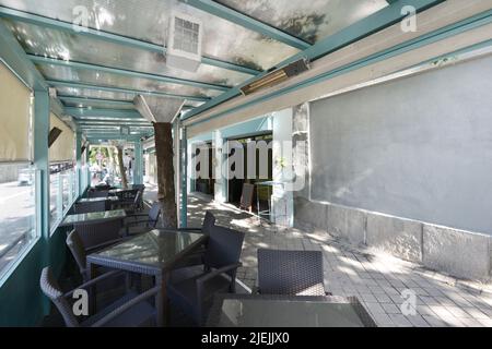 Portico di un ristorante azzurro sul marciapiede di una strada con tavoli e sedie in rattan Foto Stock