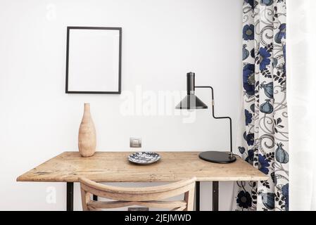 Bella scrivania vintage in legno con sedia coordinata, lampada dal design nero e tende blu sulle finestre Foto Stock