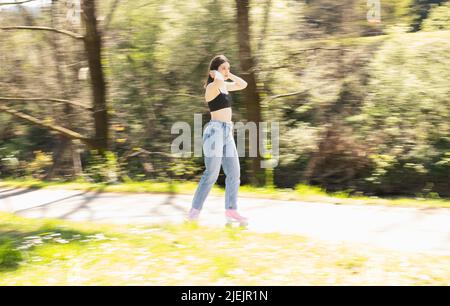 donna bruna pattinare in un parco con pattini a rotelle rosa Foto Stock