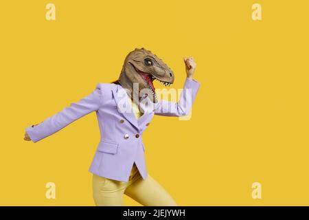 Donna pazza con t-rex maschera minacciando qualcuno con il suo pugno, copia spazio per il testo su sfondo giallo . Foto studio, ritratto. Assurdo e divertente Foto Stock