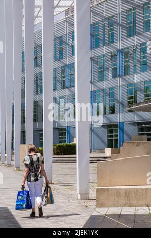 Donna che trasporta i sacchetti di shopping camminando oltre l'edificio del quadrante a Milton Keynes, Buckinghamshire, Regno Unito in giugno Foto Stock