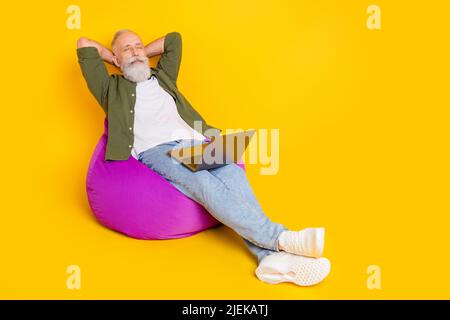 Foto del vecchio uomo sognante sit beanbag sleep hold laptop indossare camicia verde isolato colore giallo sfondo Foto Stock