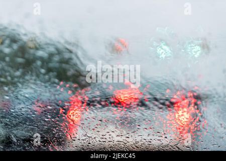 Vista astratta del colorato verde e rosso bokeh dei colori della sera del traffico sullo sfondo della luce stradale con gocce di pioggia bagnata sul cruscotto del parabrezza dell'auto Foto Stock