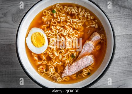 Flat TOP Lay vista primo piano di spaghetti giapponesi ramen zuppa istantanea in ciotola come pasto asiatico con consistenza di uova bollite cotte e fette di maiale condimenti galleggiano Foto Stock