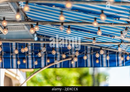 Closeup astratto di appendere lampadine giallo arancione con profondità poco profonda di campo bokeh sfondo sfocato del ristorante cafe patio coperto con il col blu Foto Stock