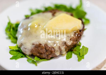 Piccolo hamburger closeup con una polpetta di hamburger e formaggio duro fuso sul letto di verde di rucola come pasto sano cheto basso-carb su piatto bianco servire Foto Stock