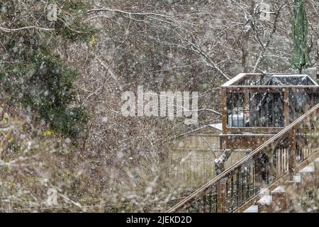 Ponte in legno con scale casa coperta di neve bianca durante la tempesta pesante nevicata da alberi di foresta con vista attraverso rami in cortile Foto Stock