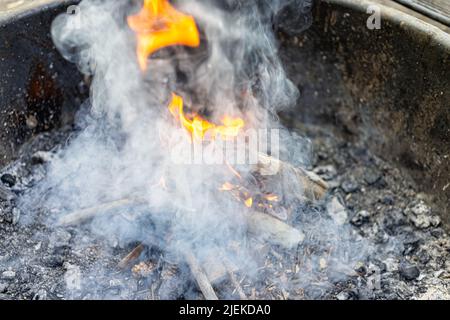 Closeup di fumo che sorge da tronchi rami di legno e fuoco che brucia lunga esposizione di fiamma arancione rosso al campeggio falò griglia firepit all'aperto par Foto Stock