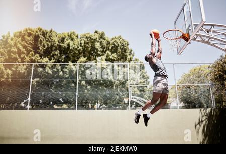 Tutta la lunghezza del giocatore di basket che cunking una sfera nella rete durante una partita su un campo. Atleta in forma e attivo che salta per segnare durante una gara Foto Stock