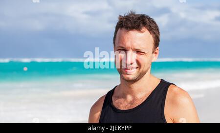 Ritratto di giovane adulto caucasico sorridente in camicia nera in piedi sulla spiaggia in una giornata estiva soleggiata, Repubblica Dominicana Foto Stock