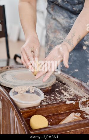Mani di giovane donna che pulisce i palmi con spugna bagnata sopra la ruota di ceramica dopo il lavoro di finitura sopra i nuovi articoli di terracotta Foto Stock