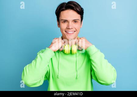 Foto di divertente attraente giovane Signore indossare felpa verde braccia sorridenti cuffie isolato blu sfondo di colore Foto Stock