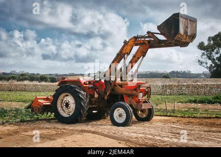 Trattore agricolo con scavatore e attrezzatura di aratura sul retro fino al suolo in un campo Foto Stock