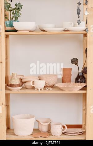 Tre mensole di legno con caraffe di argilla fatte a mano, pentole, tazze, tazze, ciotole, vasi e piatti creati e preparati per la vendita in negozio di souvenir Foto Stock