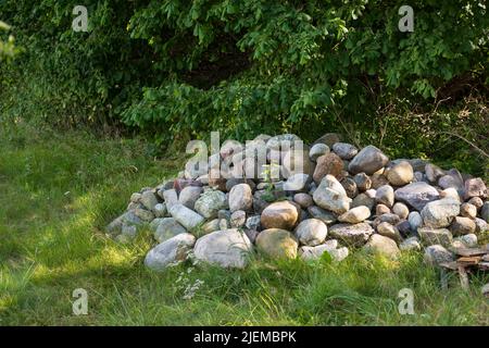 Impilato grandi pietre o rocce su un campo di erba verde. Rocce lungo un sentiero escursionistico remoto nella natura. Raccolto mucchio di pietre che marchiano terreno forestale Foto Stock