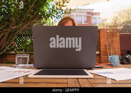 Donna telelavoro dal suo giardino con notebook e tablet. Foto Stock