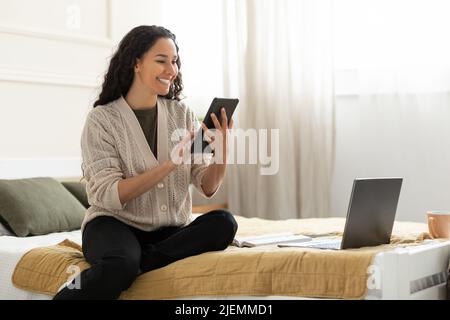 Bella giovane donna seduta a letto, lavoro sul tablet digitale a casa, spazio libero Foto Stock