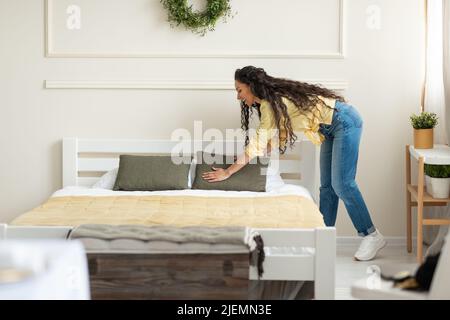 Ragazza allegra che fa il letto a casa, sistemando i cuscini, facendo i lavori di casa al mattino, spazio copia. Routine quotidiana Foto Stock
