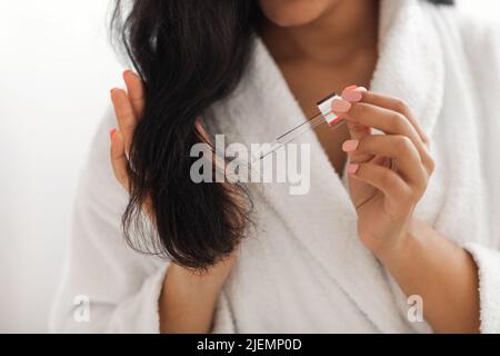 African American Woman che applica il siero sui capelli all'interno, tagliato Foto Stock