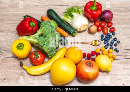 Un cucchiaio di legno con integratori alimentari viene posto al centro di frutta fresca e verdure, che vengono poste su un tavolo di legno. Integratori alimentari enab Foto Stock