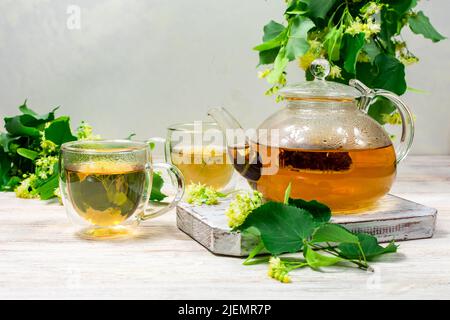 Teiera e due tazze di tè con un tiglio su un tavolo di legno. Tè healing. Foto Stock