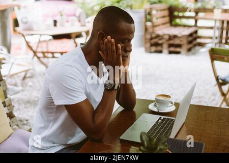 Puzzled e confuso multiculturale uomo scuro pelle usando il laptop, sedersi in un caffè all'aperto, guardando il monitor. Colloquio di lavoro Foto Stock