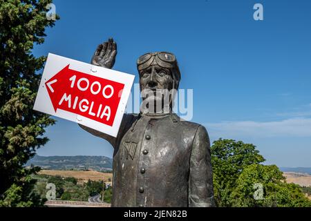 La statua commemorativa di Tazio Nuvolari con un cartello che fa pubblicità alla gara di Mille miglia, San Quirico d'Orcia, Toscana, Italia Foto Stock