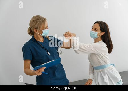 Medico indossare maschera protettiva contro il covid, elbowing toccare in saluto con il paziente Foto Stock