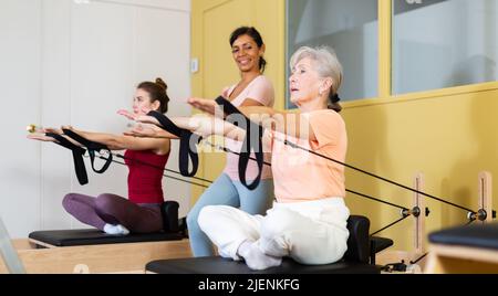 Donna anziana che fa esercizi di stretching su pilates reformer Foto Stock