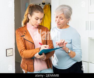 Donna anziana che risponde alle domande dell'intervistatore femminile a casa Foto Stock