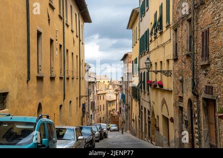 Una pittoresca strada in pendenza con auto parcheggiate nel centro medievale della cittadina collinare toscana di Volterra, Italia. Foto Stock