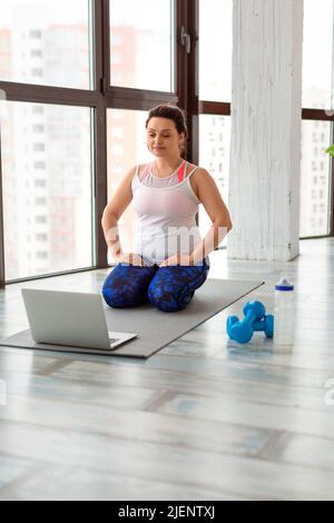 Donna di mezza età meditating. Si siede in ginocchio davanti al monitor. Concetto di stile di vita sano. Foto verticale. Foto Stock