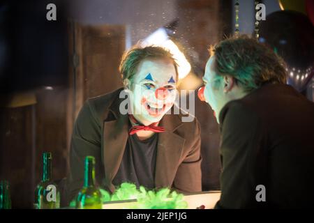 Clown concetto - un uomo pazzo clown guardando il suo specchio riflessione nello spogliatoio e ridendo Foto Stock