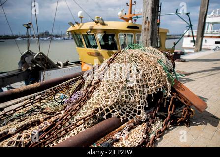 Norddeich, Germania. 25th giugno 2022. Una rete per la pesca si trova nel porto di fronte ad un taglierino da pesca sul muro della banchina. Credit: Hauke-Christian Dittrich/dpa/Alamy Live News Foto Stock