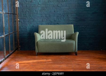 divano verde morbido vicino alla parete blu sul pavimento in legno della camera, mobili imbottiti nell'appartamento, divano nella hall, minimalismo Foto Stock