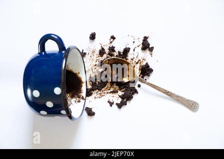 una tazza con caffè capovolto su sfondo bianco e un cucchiaino da tè si trova accanto ad esso, caffè versato su sfondo bianco Foto Stock