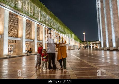 Jakarta, Indonesia. 17th giugno 2022. Una famiglia scatta una foto di gruppo intorno alla Moschea Istiqlal. L'atmosfera della città di Giacarta, Indonesia di notte, che è così affollata con varie attività. Credit: SOPA Images Limited/Alamy Live News Foto Stock