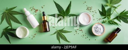 Foglie di canapa e prodotti di bellezza, olio cbd in bottiglia, crema viso e siero, medicina alternativa e concetto di cura biologica della pelle. Banner. Foto Stock