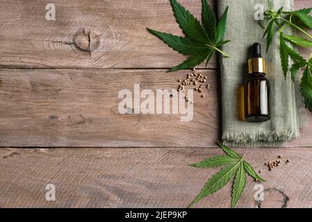 Faccia siero o bottiglia di olio di cbd e foglie verdi di pianta di canapa su sfondo di legno, spazio di copia. Medicina alternativa, olio cbd e concetto di cura organica della pelle Foto Stock