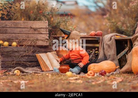 Vacanze autunnali. Una ragazza piccola carina in un costume strega è seduta nel giardino e sfogliando attraverso un libro. Concetto di Halloween. Foto Stock