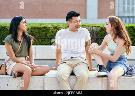 Gli amici ridono e parlano mentre si rilassano seduti all'aperto. Amicizia e stile di vita urbano. Foto Stock