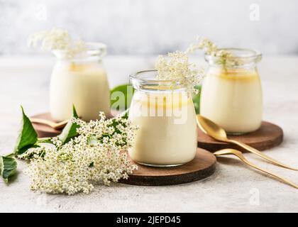 Panna cotta di fiori di sambuco cremosi fatti in casa con salsa di limone in vasetti di vetro vintage su un fondo di cemento chiaro. Foto Stock