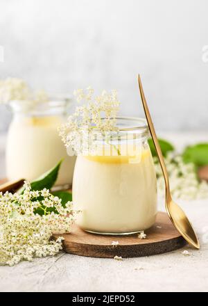 Panda cotta con fiori di sambuco, dessert alla crema con cagliata di limone in vasetti di vetro vintage su sfondo di ardesia chiaro. Concetto di cibo biologico fatto in casa. Spazio di copia Foto Stock