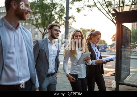 Gruppo di giovani uomini d'affari allegri che parlano tra loro mentre camminano all'aperto Foto Stock