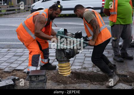 Due lavoratori esercitano un vibratore portatile per abbattere la sabbia. Concentratevi sulla sabbia e sulle pietre, la macchina ha la sfocatura delle vibrazioni Foto Stock