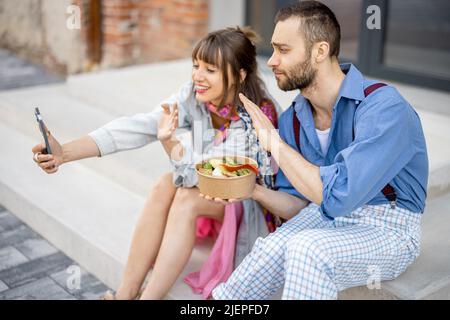 I colleghi mangiano cibo sano take away e parlano al telefono all'aperto Foto Stock