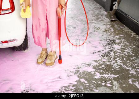 La donna si alza sulla schiuma rosa mentre lava la sua auto Foto Stock