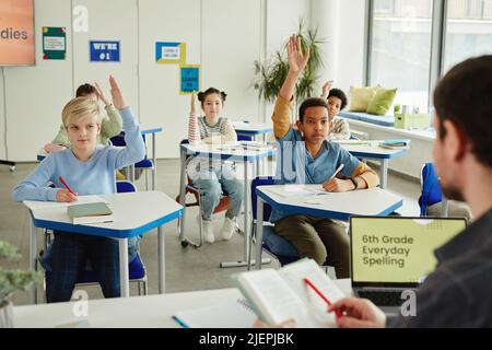 Gruppo diversificato di bambini che alzano le mani in classe e rispondono alle domande sull'ortografia Foto Stock