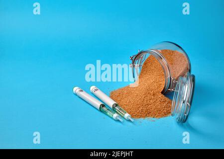 Penne per siringhe per insulina e un vaso di vetro con zucchero di canna sparso su sfondo blu con spazio per la copia Foto Stock